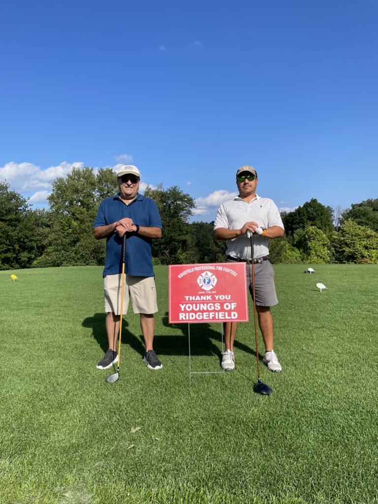 Two men standing in a golf course, each holding a golf club.