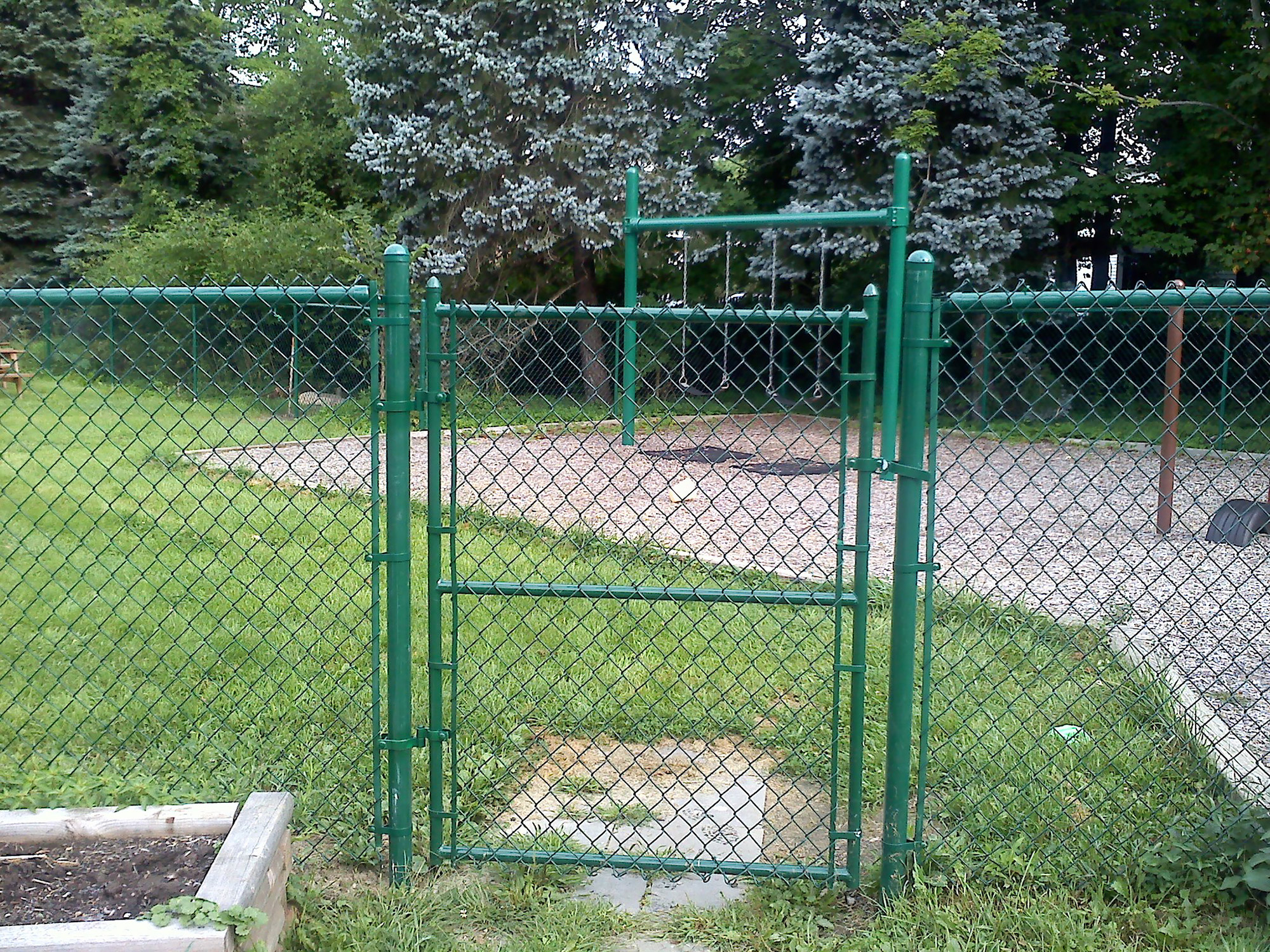 A green gate in a fenced area, safeguarded by chain link.