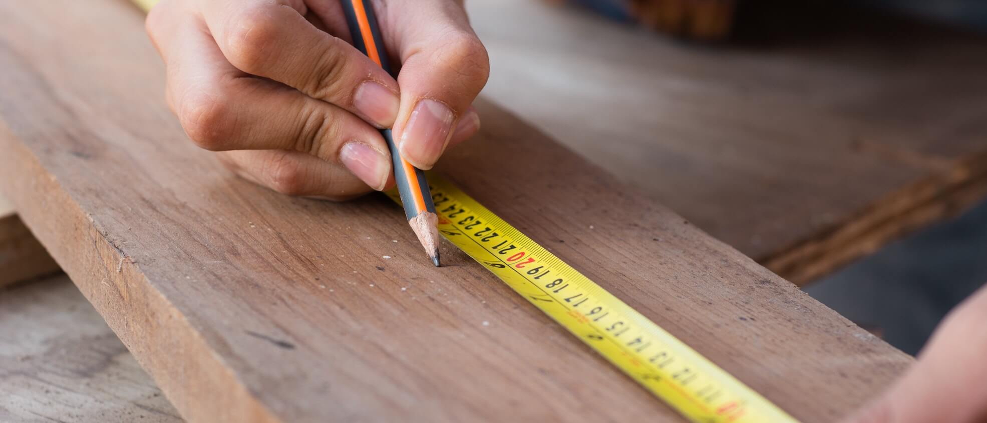 A fence contractor measuring wood with a tape measure.