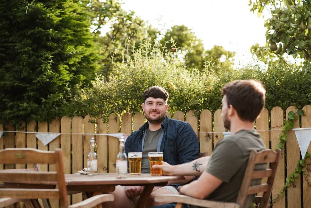 Two men seated at a table in a modern backyard setting.
