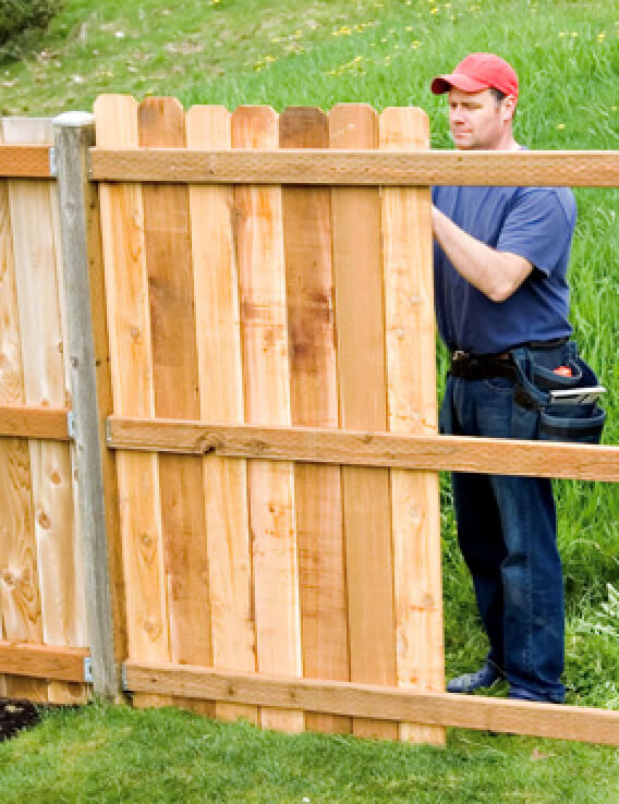 Photo of a man building a wooden fence in a field.