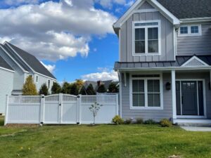 Photo of a grey colored house with a white vinyl fence to the left.